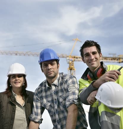 Three people on a construction site. The woman is wearing a white hard hat, the man in the middle is wearing a blue hard hat, and the man on the right is wearing a high vis vest and holding a phone and a white hard hat. image for financial wellness consulting for nonprofits and companies.